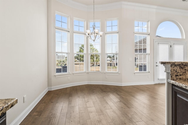 unfurnished dining area featuring dark wood-style floors, a chandelier, ornamental molding, and baseboards