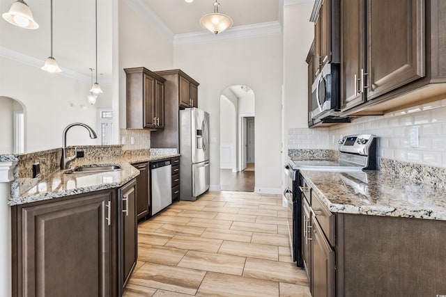 kitchen with arched walkways, dark brown cabinetry, stainless steel appliances, a peninsula, and a sink