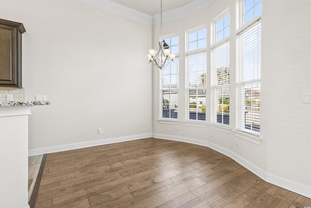 unfurnished dining area featuring an inviting chandelier, baseboards, crown molding, and wood finished floors