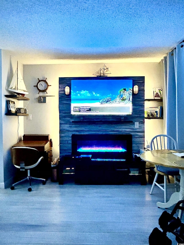 living area with a glass covered fireplace, a textured ceiling, and wood finished floors