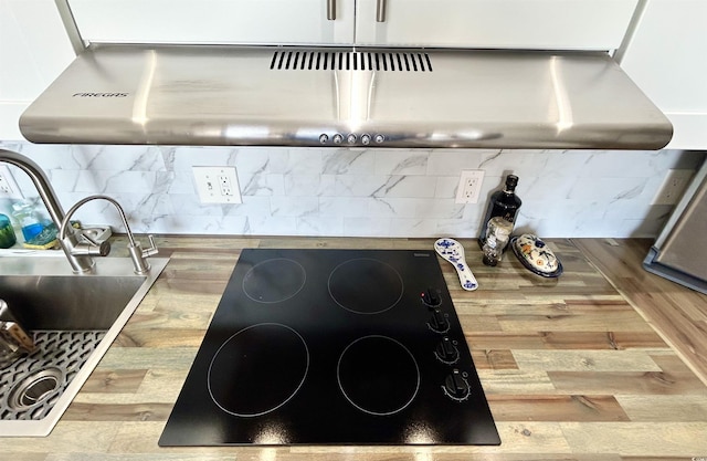 interior details featuring under cabinet range hood, black electric stovetop, backsplash, and a sink