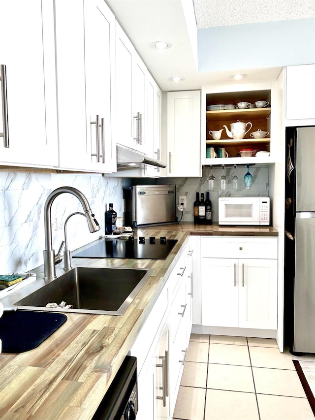 kitchen featuring white microwave, white cabinetry, freestanding refrigerator, and light tile patterned flooring