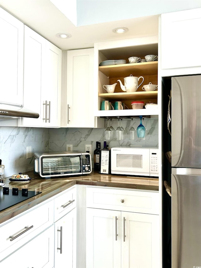 kitchen with white microwave, decorative backsplash, white cabinetry, and freestanding refrigerator