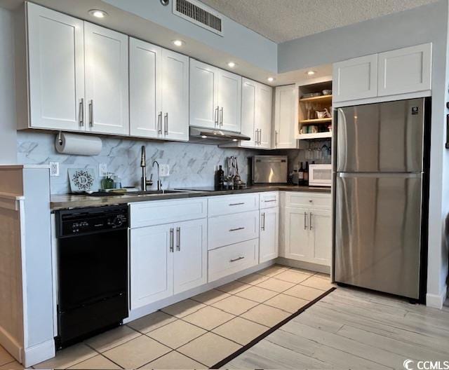 kitchen featuring dark countertops, visible vents, under cabinet range hood, black dishwasher, and freestanding refrigerator