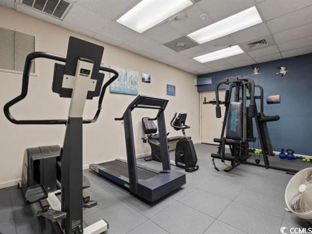 exercise room featuring visible vents, a paneled ceiling, and baseboards