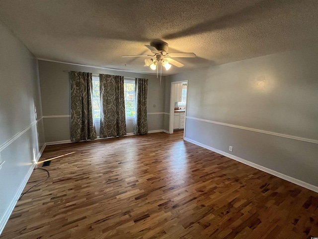 empty room with dark wood-style floors, a textured ceiling, a ceiling fan, and baseboards