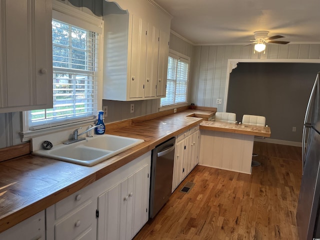 kitchen with appliances with stainless steel finishes, white cabinets, a sink, and wood finished floors