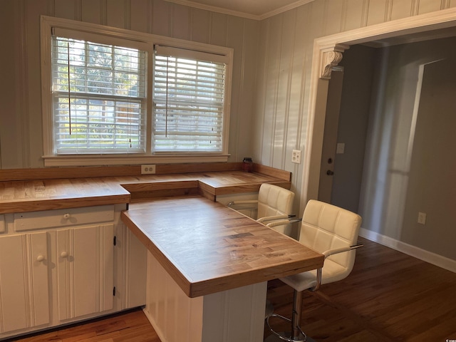 interior space featuring baseboards, ornamental molding, wooden counters, and wood finished floors