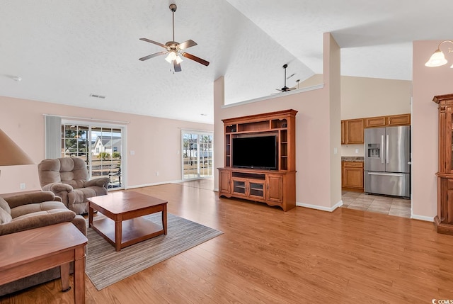 living room with baseboards, a ceiling fan, a textured ceiling, light wood-style floors, and high vaulted ceiling