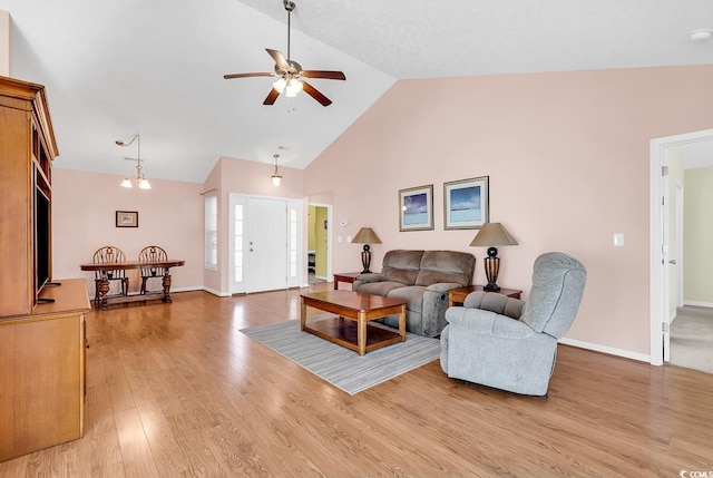 living room with ceiling fan with notable chandelier, high vaulted ceiling, light wood-type flooring, and baseboards