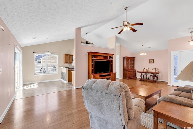 living area with a textured ceiling, light wood-style flooring, lofted ceiling, and a ceiling fan