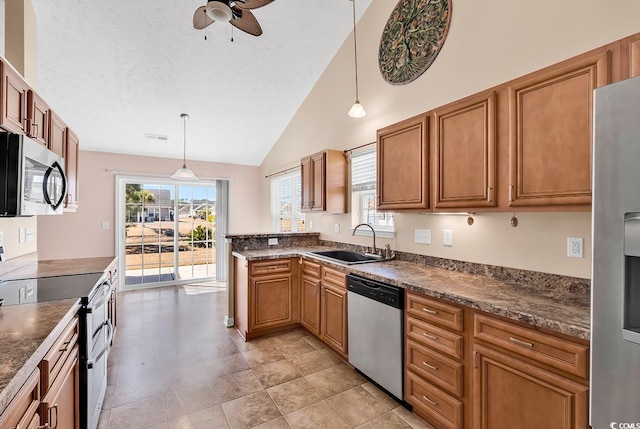 kitchen with a sink, appliances with stainless steel finishes, brown cabinetry, dark countertops, and decorative light fixtures