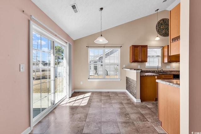 kitchen with vaulted ceiling, visible vents, brown cabinets, and pendant lighting