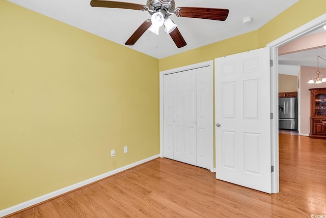 unfurnished bedroom featuring a closet, light wood-type flooring, stainless steel fridge, baseboards, and ceiling fan with notable chandelier