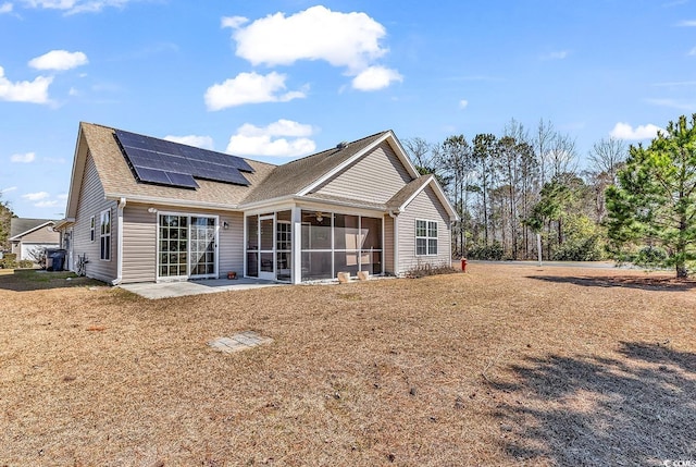 rear view of property with a shingled roof, a sunroom, and roof mounted solar panels