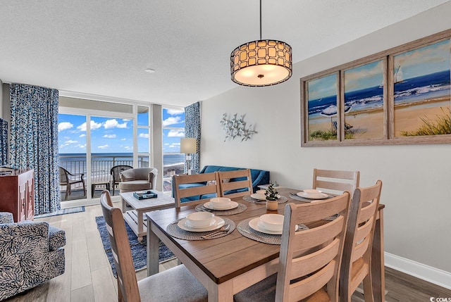 dining space with baseboards, wood finished floors, a water view, a textured ceiling, and floor to ceiling windows