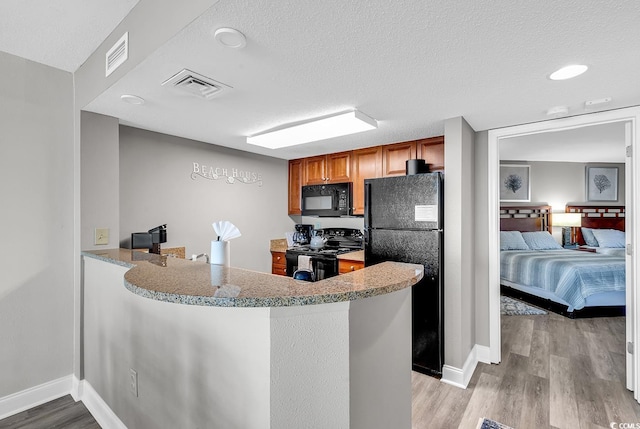 kitchen with a textured ceiling, visible vents, brown cabinets, black appliances, and light wood finished floors