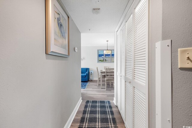 corridor with a textured wall, a textured ceiling, baseboards, and wood finished floors