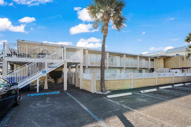 view of building exterior with uncovered parking, stairway, and fence