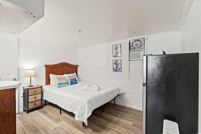 bedroom with light wood-style floors, freestanding refrigerator, and radiator heating unit