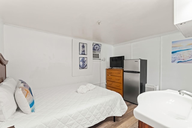 bedroom with freestanding refrigerator, radiator, crown molding, and wood finished floors