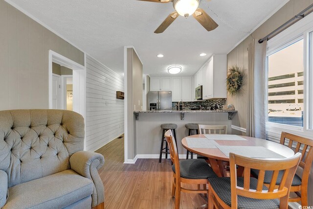 9501 Shore Dr Unit D-132, Myrtle Beach, SC 29572 - dining room featuring light wood finished floors, a ceiling fan, ornamental molding, wooden walls, and a textured ceiling