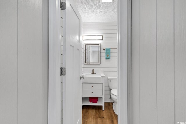 9501 Shore Dr Unit D-132, Myrtle Beach, SC 29572 - half bathroom featuring a textured ceiling, toilet, wooden walls, wood finished floors, and vanity