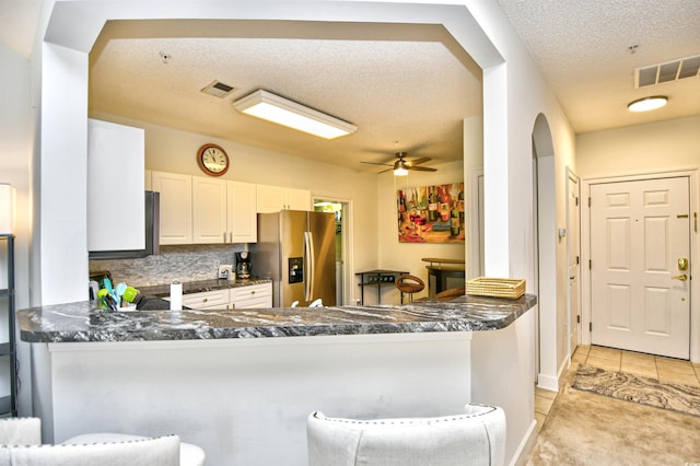 kitchen with dark countertops, light tile patterned floors, a peninsula, and stainless steel refrigerator with ice dispenser