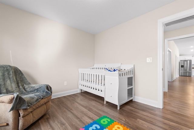 bedroom featuring baseboards, visible vents, wood finished floors, and stainless steel fridge with ice dispenser