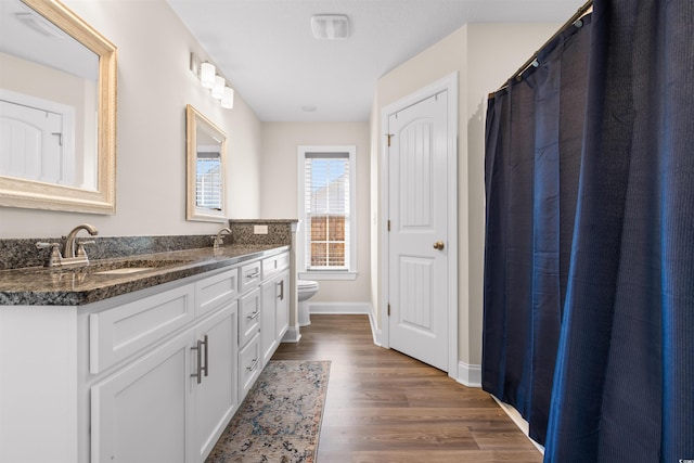 bathroom featuring double vanity, baseboards, toilet, wood finished floors, and a sink