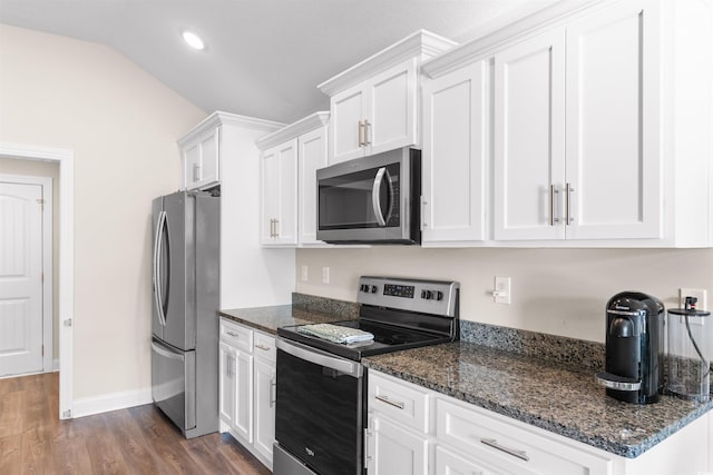 kitchen with dark stone counters, dark wood-style floors, vaulted ceiling, stainless steel appliances, and white cabinetry