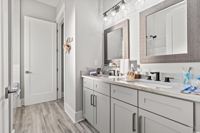 full bathroom with a sink, baseboards, wood finished floors, and double vanity