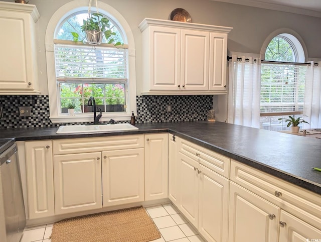 kitchen with white cabinets, decorative backsplash, dark countertops, a sink, and stainless steel dishwasher