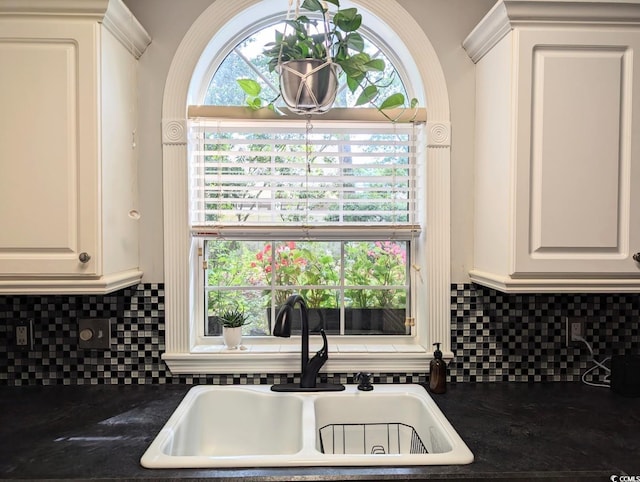 kitchen with dark countertops, a sink, white cabinetry, and decorative backsplash