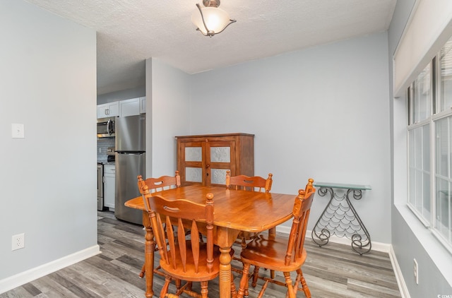 dining room with baseboards, a textured ceiling, and light wood finished floors