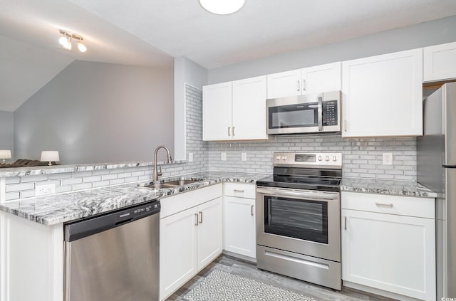 kitchen with a peninsula, white cabinetry, stainless steel appliances, and a sink