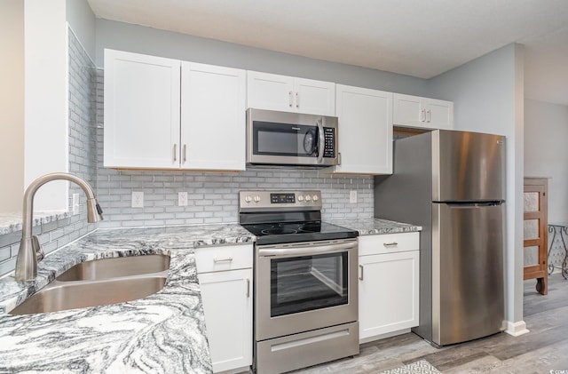 kitchen with light stone counters, a sink, white cabinets, appliances with stainless steel finishes, and tasteful backsplash