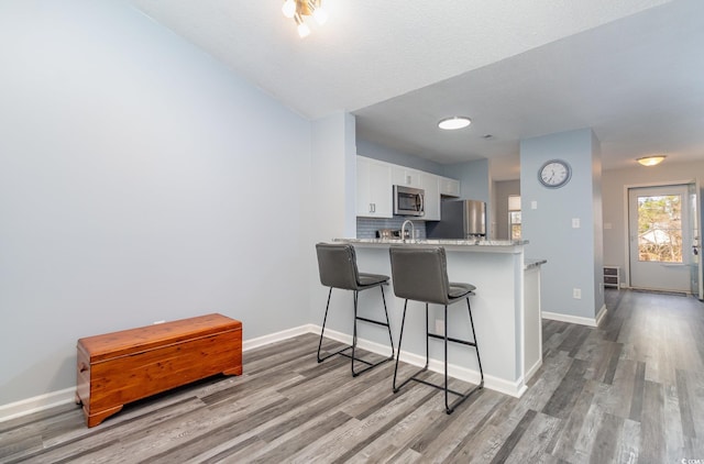 kitchen with stainless steel microwave, a kitchen breakfast bar, fridge, white cabinetry, and backsplash