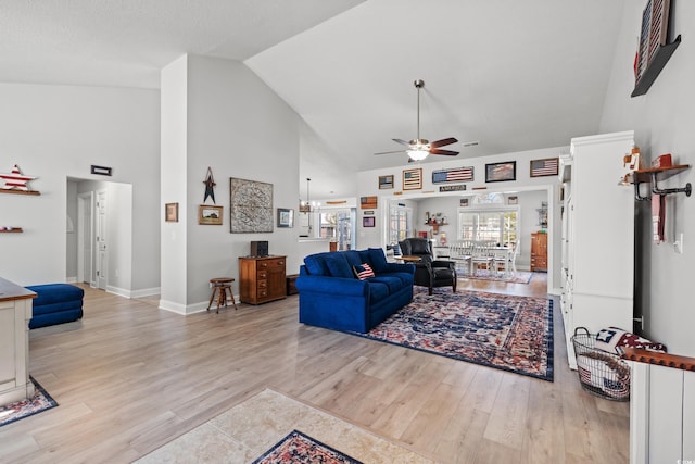 living area featuring light wood-type flooring, baseboards, high vaulted ceiling, and ceiling fan with notable chandelier