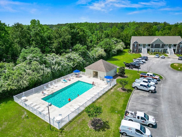 community pool with a forest view, a yard, fence, and a patio