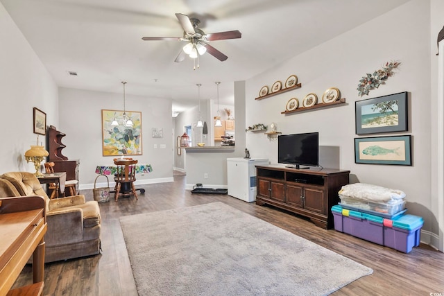 living area featuring baseboards, visible vents, wood finished floors, and ceiling fan with notable chandelier