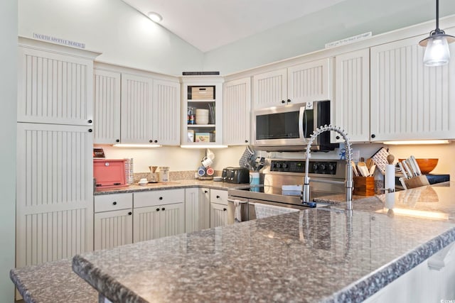 kitchen with dark stone counters, hanging light fixtures, vaulted ceiling, stainless steel appliances, and white cabinetry