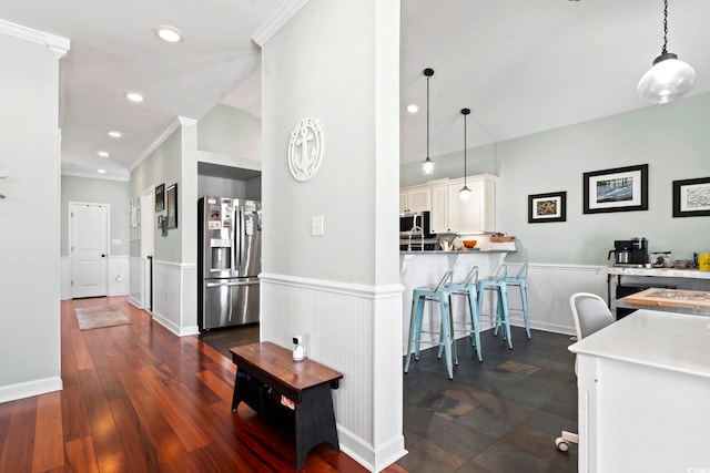 kitchen featuring a wainscoted wall, white cabinetry, appliances with stainless steel finishes, and crown molding