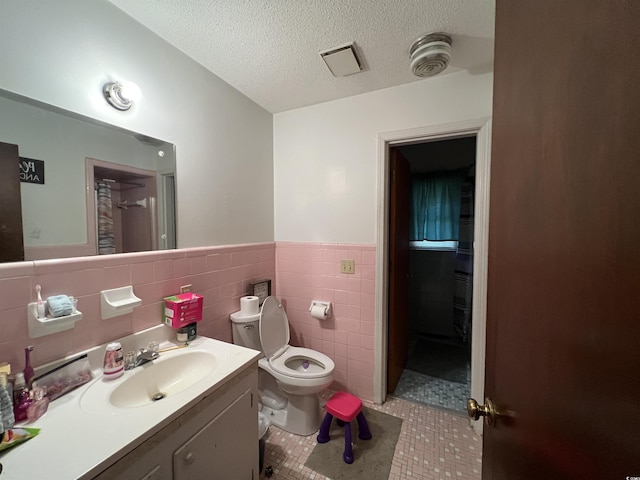 full bathroom with tile walls, toilet, a textured ceiling, vanity, and tile patterned flooring