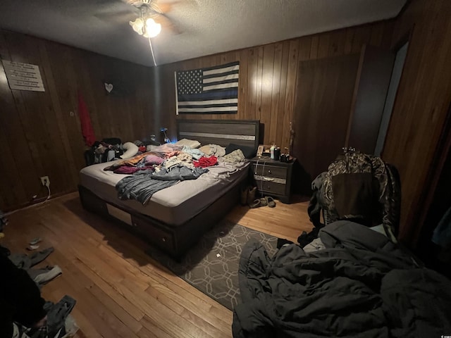 bedroom with a textured ceiling, wood finished floors, a ceiling fan, and wooden walls