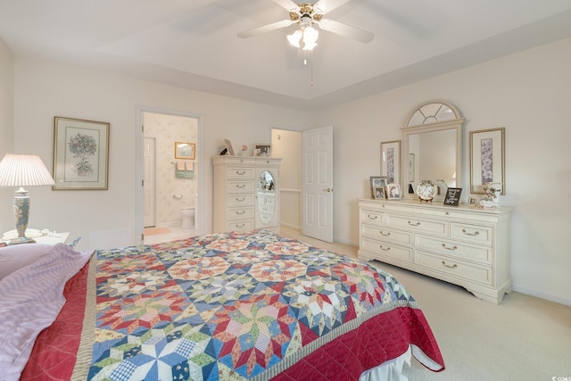 bedroom with light colored carpet, a ceiling fan, baseboards, a tray ceiling, and ensuite bath