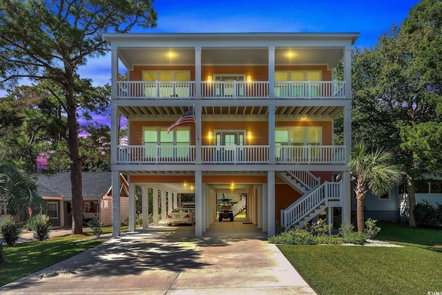 beach home featuring concrete driveway, covered porch, a balcony, a carport, and stairs