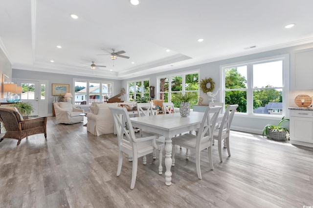 dining room with light wood-type flooring, a tray ceiling, a healthy amount of sunlight, and visible vents