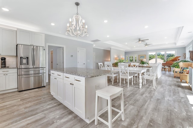 kitchen featuring a raised ceiling, crown molding, light wood-type flooring, stainless steel refrigerator with ice dispenser, and backsplash