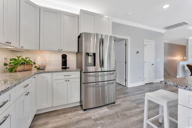 kitchen featuring light wood-style flooring, visible vents, stainless steel refrigerator with ice dispenser, decorative backsplash, and crown molding